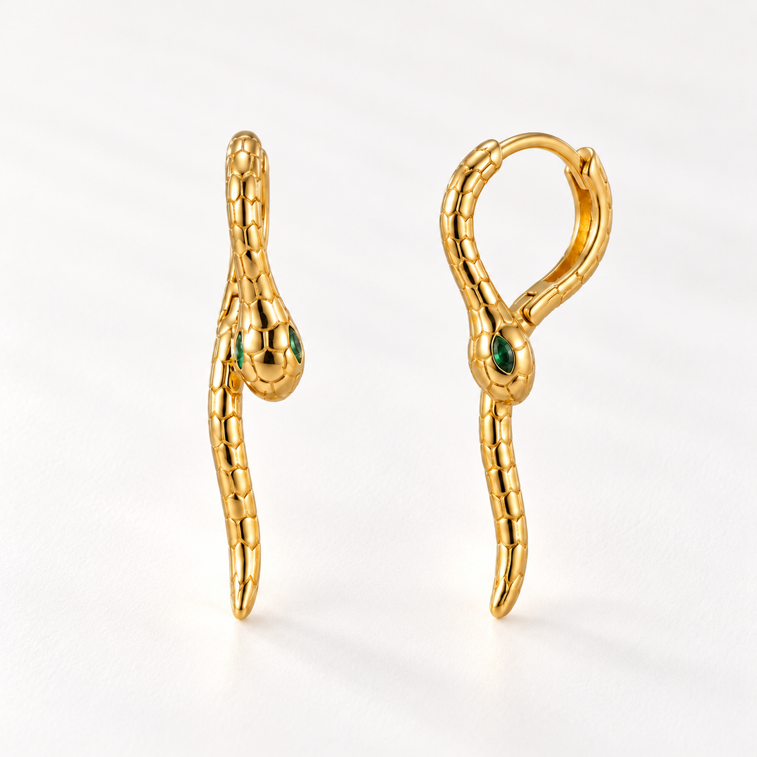 A pair of 18k gold snake-shaped huggie hoop earrings with emerald green stone eyes, shown from front and side angles on a clean white background displaying the textured scale detail and hinged closure.