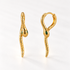 A pair of 18k gold snake-shaped huggie hoop earrings with emerald green stone eyes, shown from front and side angles on a clean white background displaying the textured scale detail and hinged closure.