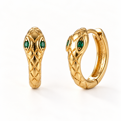 A pair of 18k gold snake-shaped huggie hoop earrings with emerald green stone eyes and textured scale pattern, shown from front and side angles on a clean white background displaying the hinged closure and detailed serpent head design.