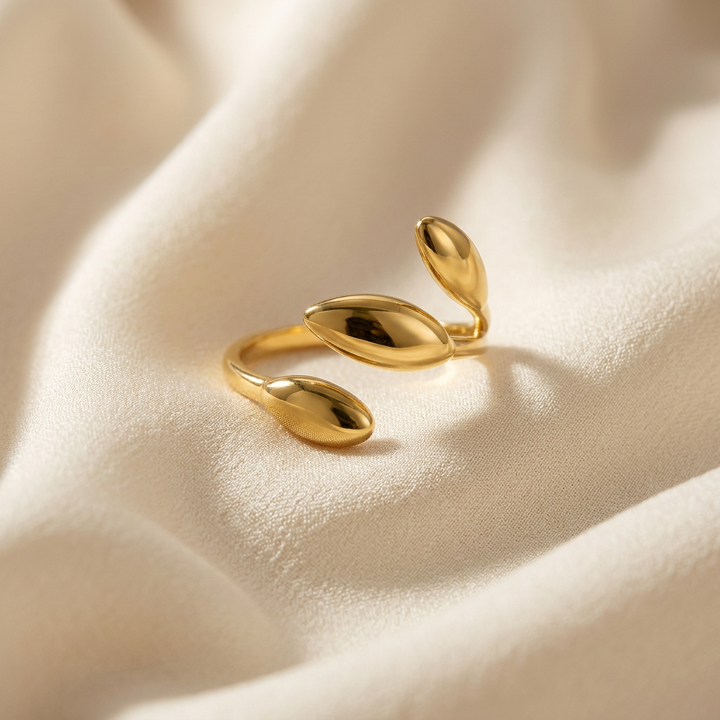 A gold sprout leaf ring with three oval botanical leaves emerging from open adjustable band lying flat on a white background with soft natural shadows, showing the nature-inspired growth symbolism, sculptural leaf forms, and polished gold finish from above.