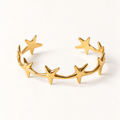 A gold star cuff bracelet with multiple five-point stars forming an open celestial band, shown from front and side angles on a clean white background displaying the polished star shapes, open cuff design, and cosmic constellation aesthetic.
