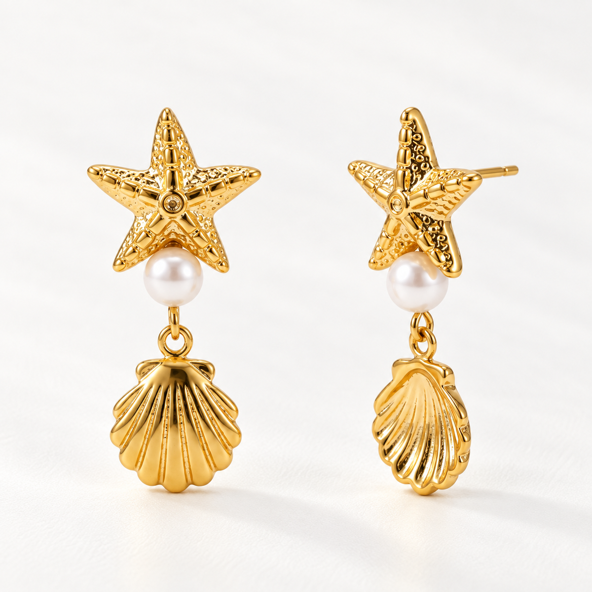 A pair of 18k gold starfish stud earrings with white pearl centers and dangling scallop shell charms, shown from front and side angles on a clean white background displaying the textured sea-inspired details and post with butterfly backing.