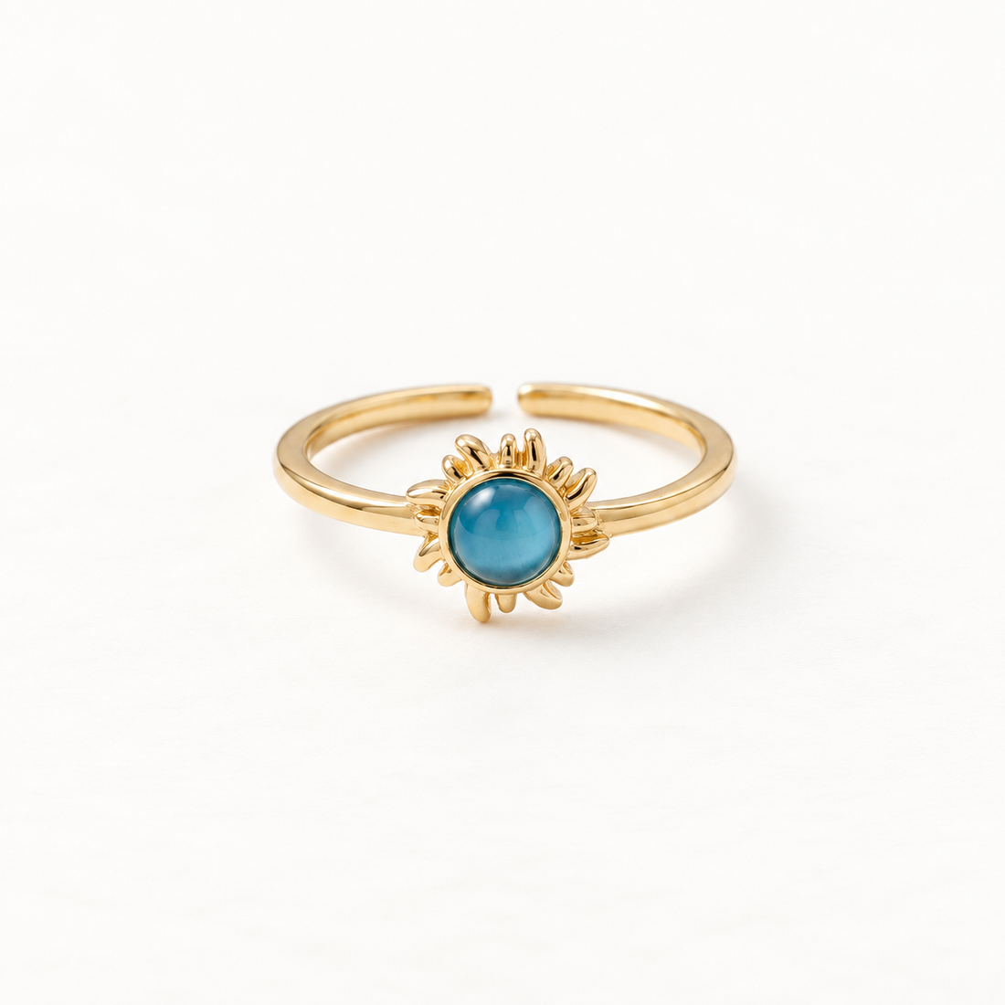 A gold sun ring with vibrant blue turquoise center stone and radiating sunburst rays, celestial open adjustable band with textured edges, shown from front and side angles on a clean white background displaying the bright blue hue, detailed ray texture, and polished gold finish.