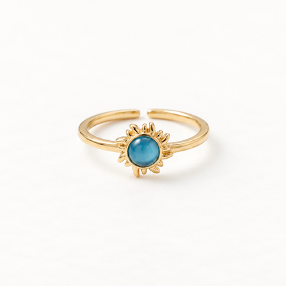 A gold sun ring with vibrant blue turquoise center stone and radiating sunburst rays, celestial open adjustable band with textured edges, shown from front and side angles on a clean white background displaying the bright blue hue, detailed ray texture, and polished gold finish.