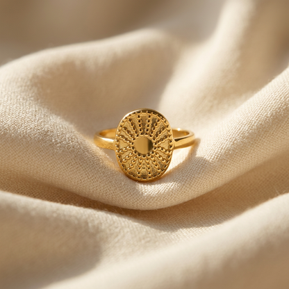 A gold sun coin filigree ring with intricate radiating pattern and smooth polished center lying flat on a white background with soft natural shadows, showing the ornate celestial symbolism, delicate ray texture, and polished gold finish from above.