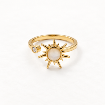 A gold sun ring with iridescent mother of pearl center stone and radiating rays, small clear crystal accent on band, open adjustable design, shown from front and side angles on a clean white background displaying the luminous pearl center, celestial symbolism, and polished gold finish.