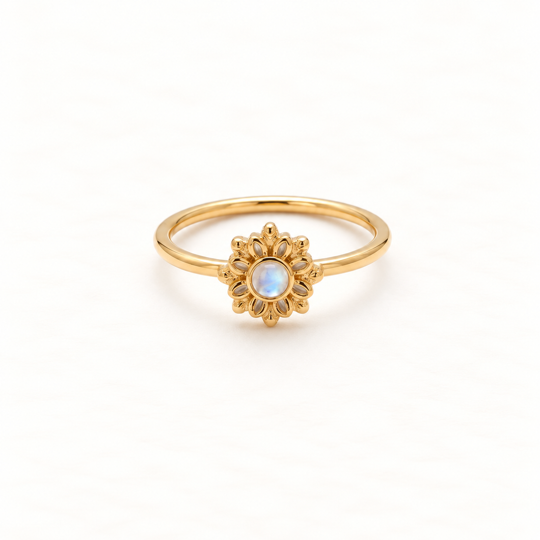 A gold sunburst flower ring with radiating petal design and central iridescent moonstone, delicate slim band, shown from front and side angles on a clean white background displaying the celestial bloom symbolism, detailed petal texture, and polished gold finish.
