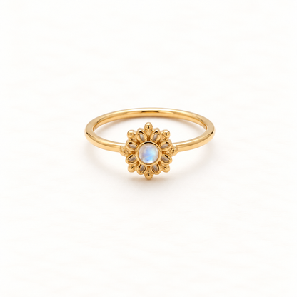 A gold sunburst flower ring with radiating petal design and central iridescent moonstone, delicate slim band, shown from front and side angles on a clean white background displaying the celestial bloom symbolism, detailed petal texture, and polished gold finish.