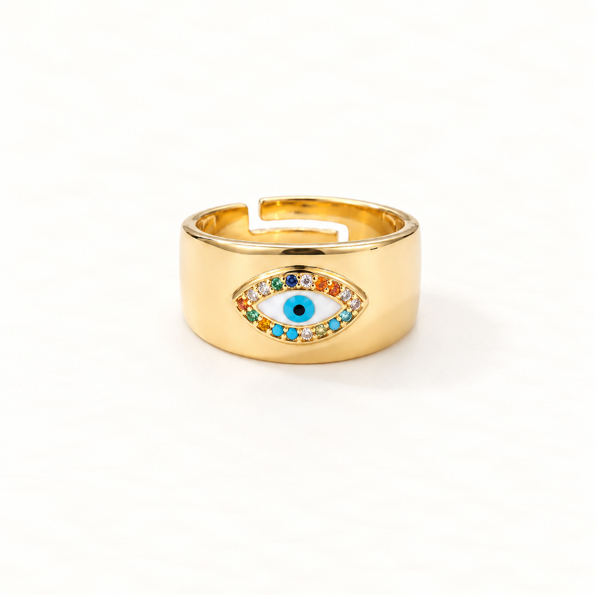 A gold wide band evil eye ring with thick statement band, multi-colored rainbow crystals surrounding deep blue center stone, bold protective symbol design, open adjustable band, shown from front and side angles on a clean white background displaying the vibrant stone detail, substantial presence, and polished gold finish.
