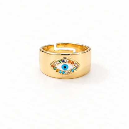 A gold wide band evil eye ring with thick statement band, multi-colored rainbow crystals surrounding deep blue center stone, bold protective symbol design, open adjustable band, shown from front and side angles on a clean white background displaying the vibrant stone detail, substantial presence, and polished gold finish.